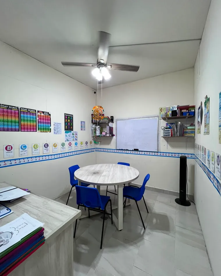 Sala de tutorías con mesa redonda, sillas azules y pizarrón.